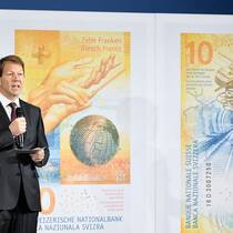 SNB-Vizedirektor Fritz Zurbrügg präsentiert den 10-Franken-Schein: Auf dem neuen Zehner dreht sich alles das Organisationstalent der Schweiz. Auf der Vorderseite ist ein Globus mit den Zeitzonen zu sehen, auf der Rückseite ist ein Uhrwerk abgebildet. Ebenfalls zu sehen ist ein Eisenbahntunnel, der laut Zurbrügg für die Schweizer Ingenieurskunst stehen soll.