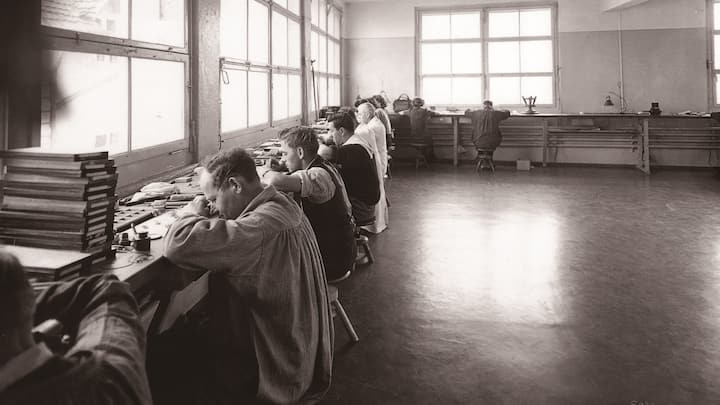 Uhrenmacher arbeiten nebeneinander vor einer Fensterfront in der Felca-Manufaktur, ca. 1920.