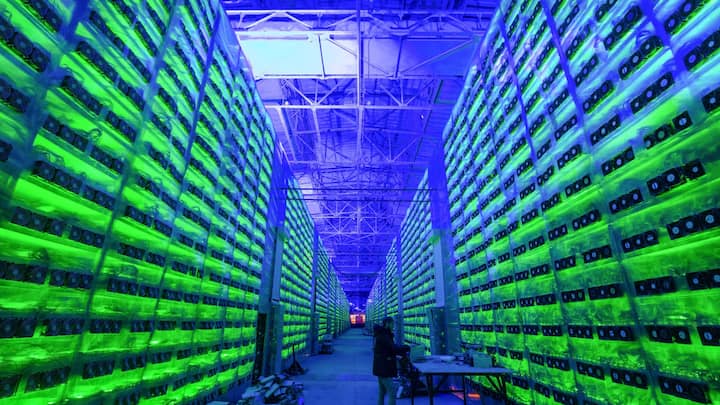 A worker inspects hardware devices as illuminated mining rigs operate inside racks at the CryptoUniverse cryptocurrency mining farm in Nadvoitsy, Russia, on Thursday, March 18, 2021. The rise of Bitcoin and other cryptocurrencies has prompted the greatest push yet among central banks to develop their own digital currencies. Photographer: Andrey Rudakov/Bloomberg