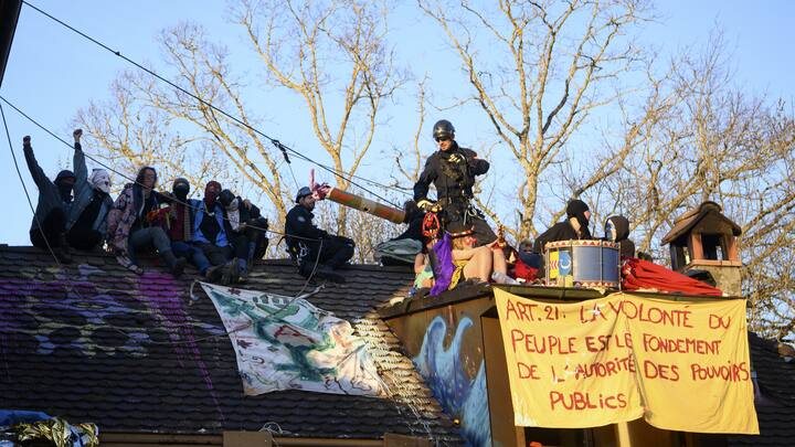 Environmental activists stand oin the roof of the house as Swiss police officers try to arrest them during the operation of the eviction of environmental protesters from the ZAD de la Colline "Zone A Defendre" (zone to defend) installed by environmental activists in the the so-called "plateau de la Birette" to block the extension of the Mormont quarry operated by the cement company LafargeHolcim between Eclepens and La Sarraz, Switzerland, Tuesday, March 30, 2021 (KEYSTONE/Jean-Christophe Bott)