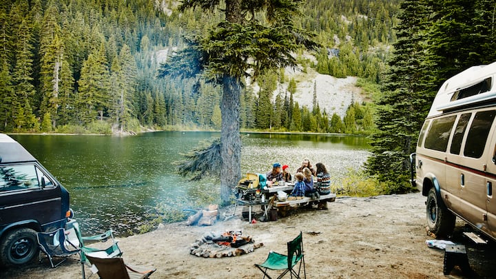 Family and friends sharing a meal together at campsite by lake in mountains