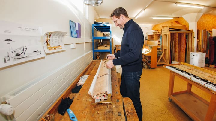 János Horváth arbeitet an Klaviertasten, die auf einer holzigen Werkbank liegen.