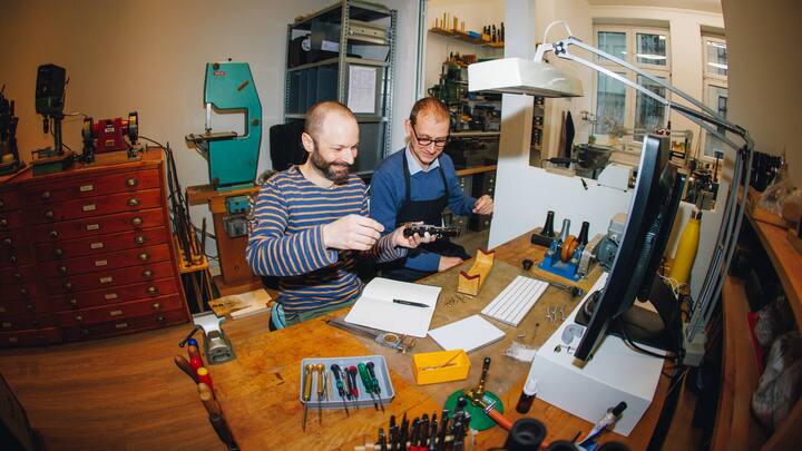 Zwei Instrumentenbauer sitzen an einem Tisch in der Werkstatt und werkeln an einem Klarinettenstück.
