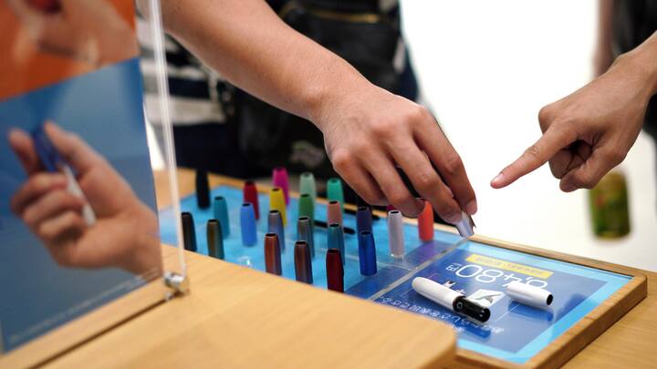 In this Oct. 22, 2018 photo, visitors look at a pen-like "heat-not-burn" device iQOS at an IQOS store in Tokyo. In Japan, Philip Morris opened nine iQOS stores in trendy districts nationwide, offering free WiFi and drinks, to perk consumer interest. (AP Photo/Eugene Hoshiko)