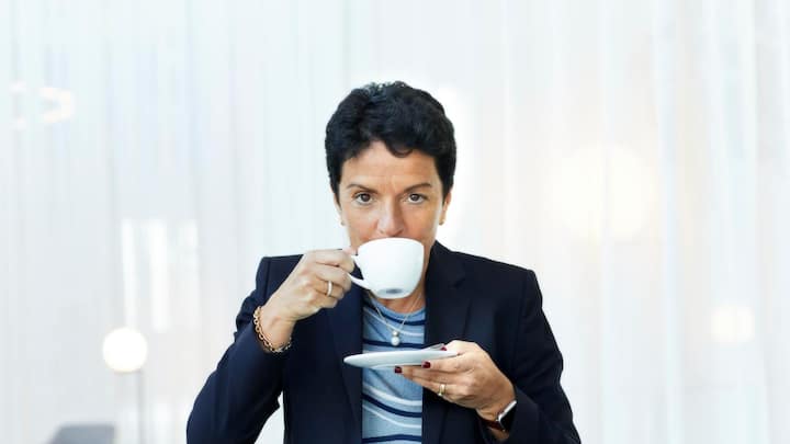 Porträt von Sabrina Soussan in schwarzem Blazer beim Kaffeetrinken.