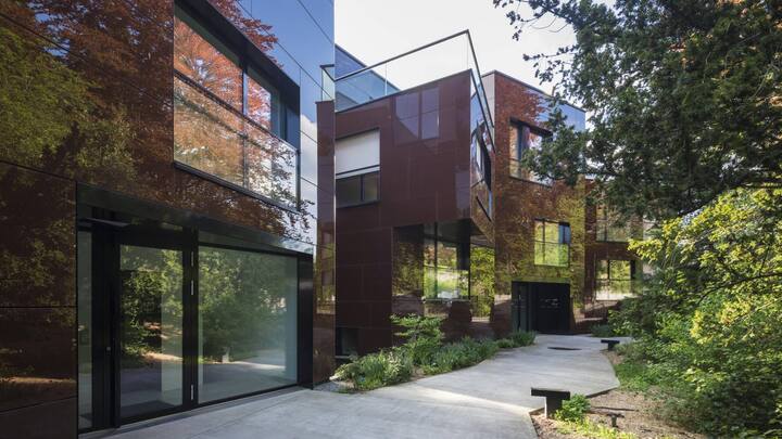 Wohnhäuser Zollikerstrasse in Zürich. Dunkelbraun emaillierte Glasplatten an der Fassade spiegeln die alten Buchen, Kiefern und Mammutbäume.