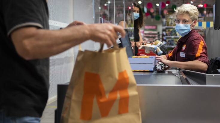 Ein Kunde mit einem Migros-Papiersack bezahlt bei der Kassierin seine Einkäufe in der Migros Crissier.