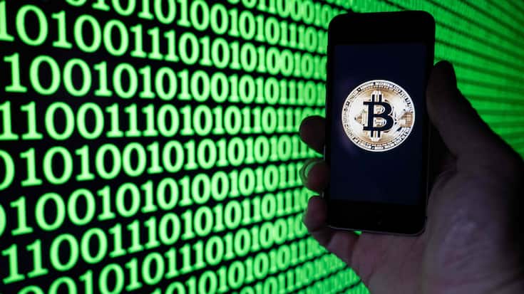 This illustration photograph shows a man holding a phone displaying a Bitcoin logo, in Mulhouse on December 5, 2025. (Photo by SEBASTIEN BOZON / AFP)