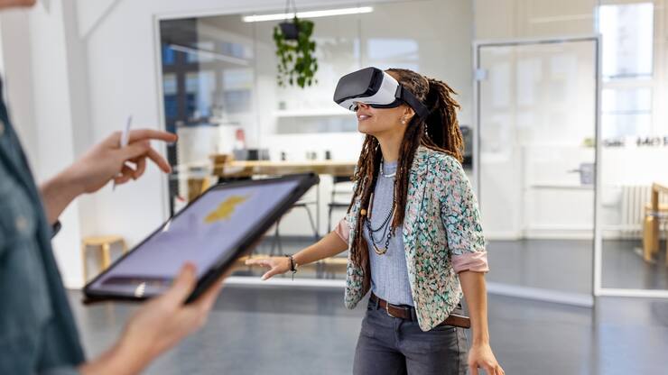 Young woman wearing virtual reality headset by a male colleague using digital tablet. Startup business colleagues testing out virtual reality glasses in the office.