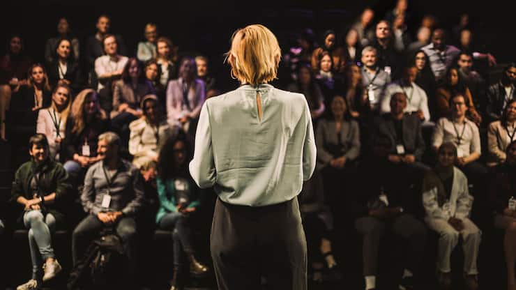 Eine Frau steht auf einer Bühen und spricht zum Publikum.