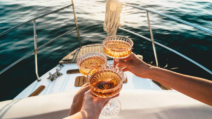 A close-up shot of friends clinking sparkling wine glasses at sunset on a yacht. Refreshing cocktail drinks. Summer outdoor parties and celebrations concepts