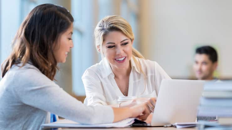 Diverse female college students review something on a laptop while studying for an exam.
