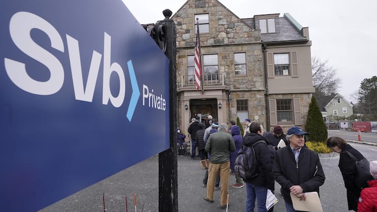FILE - Customers and bystanders form a line outside a Silicon Valley Bank branch location, Monday, March 13, 2023, in Wellesley, Mass. The sudden crisis in the U.S. banking industry is sure to cause some tightening of lending and credit and a slowdown in the pace of borrowing and spending. If it does, the crisis could actually end up aiding the Federal Reserve in the elusive goal the Fed has been pursuing for a full year: A much lower inflation rate. (AP Photo/Steven Senne, File)