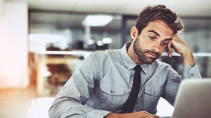 Shot of a handsome young businessman looking bored while working on a laptop in an office