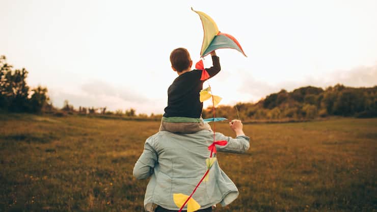 Little boy is running a kite with his father, on a beautiful day they are spending outdoors in nature