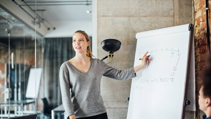 Confident businesswoman writing on flip chart in meeting at creative office
