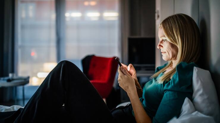 Businesswoman reclining on a hotel bed using her smartphone.