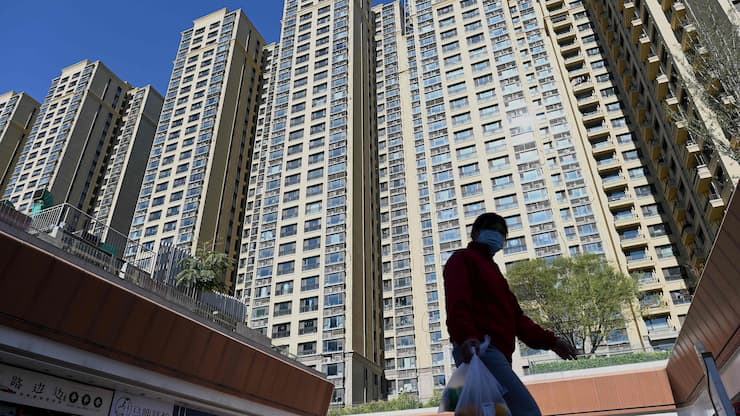 A woman walks in front of a housing complex by Chinese property developer Evergrande in Beijing on October 21, 2021. (Photo by Noel Celis / AFP)