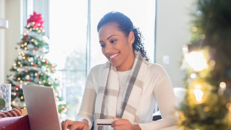 Eine Frau sitzt am Tisch und schaut lächelnd in ihren Laptop, dahinter ein Weihnachtsbaum.