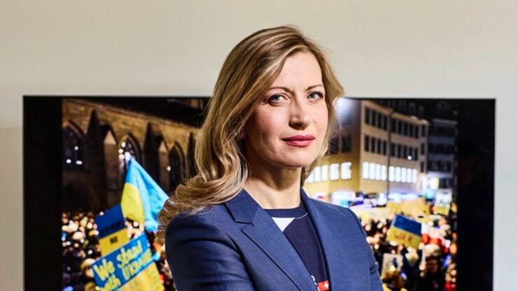 Die Ukrainerin Olga Feldmeier wurde von Forbes als "Krypto-Queen" gefeiert, nun bangt sie um ihre Familie und organisiert von ihrem Wohnort aus Hilfsaktionen. Im Hintergrund eine Aufnahme der Antikriegsdemo von ihrem Mann.