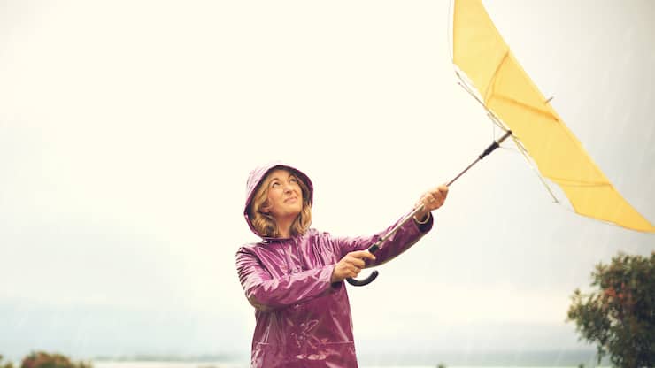 Shot of a woman standing outside in the rain holding an umbrella looking up in the sky