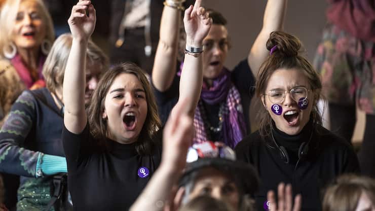 Des femmes font le signe du feminisme avec les mains, et brandissent des pancartes, lors d'une action collective organisee durant les Assises nationales pour la greve feministes et des femmes, ce dimanche 10 mars 2019 a la Maison du Peuple, a Bienne. (KEYSTONE/Adrien Perritaz)