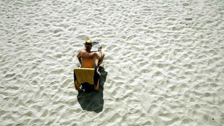 Von viel Sand umgeben sitzt dieser Mann alleine an einem Strand. Luftaufnahme.