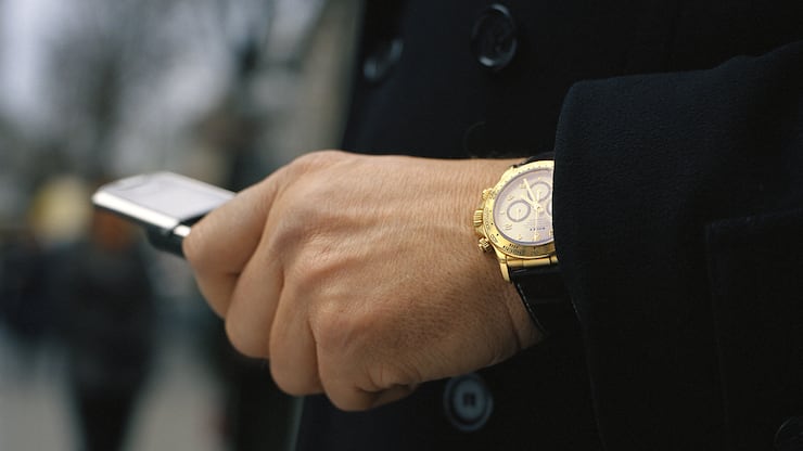 goldene Rolex Daytona am Handgelenk eines Mannes mit schwarzem Mantel