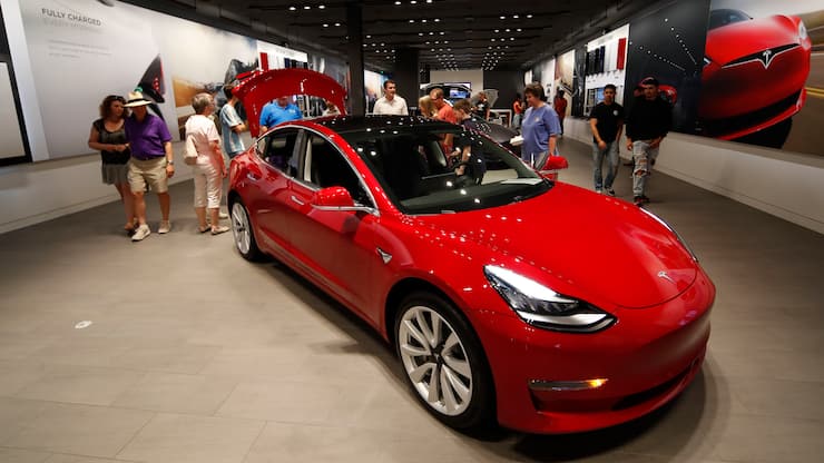 FILE- In this July 6, 2018, file photo prospective customers confer with sales associates as a Model 3 sits on display in a Tesla showroom in the Cherry Creek Mall in Denver. Tesla Inc. reports earnings on Wednesday, Oct. 24. (AP Photo/David Zalubowski, File)
