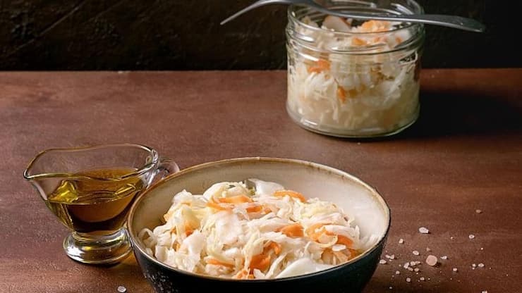 Traditional Appetizer Sauerkraut Cabbage with Carrots In Bowl and Jar. Sea Salt. Olive Oil. and Fork Nearby. Healthy Food. Fermented Products. Brown Textured Table