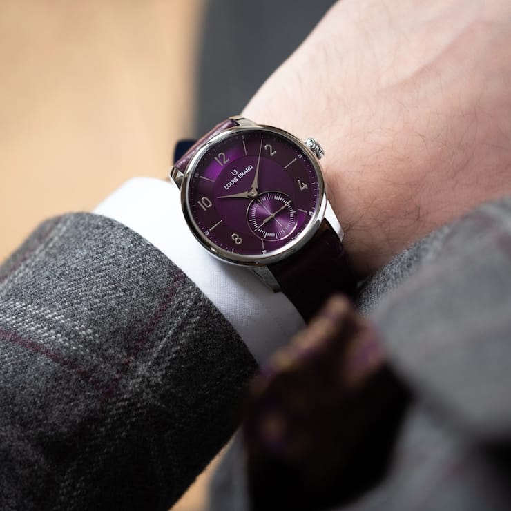 Violette Uhr von Louis Erard am Handgelenk eines Mannes.