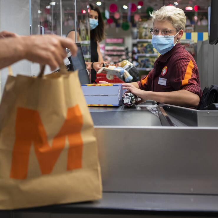 Ein Kunde mit einem Migros-Papiersack bezahlt bei der Kassierin seine Einkäufe in der Migros Crissier.