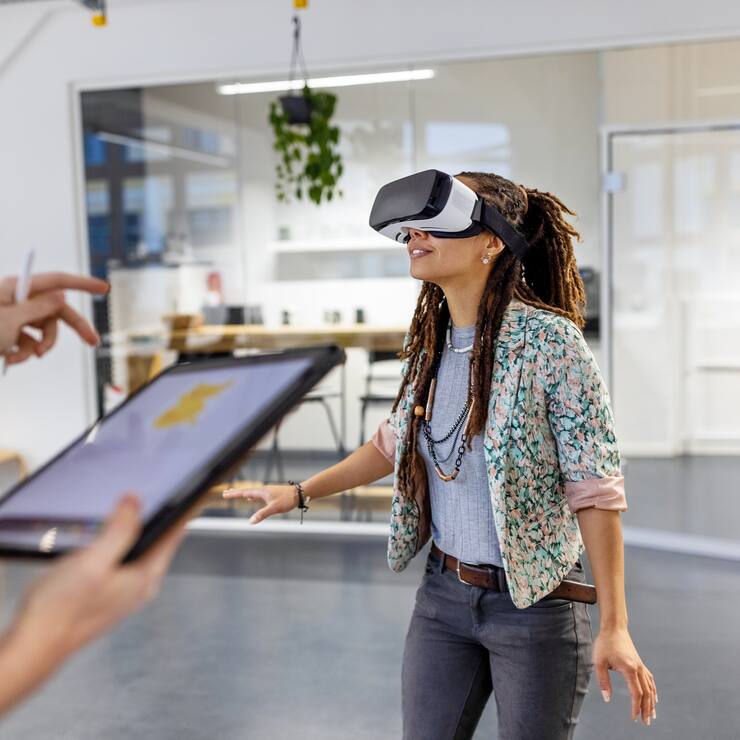 Young woman wearing virtual reality headset by a male colleague using digital tablet. Startup business colleagues testing out virtual reality glasses in the office.