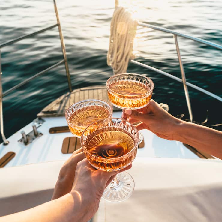 A close-up shot of friends clinking sparkling wine glasses at sunset on a yacht. Refreshing cocktail drinks. Summer outdoor parties and celebrations concepts