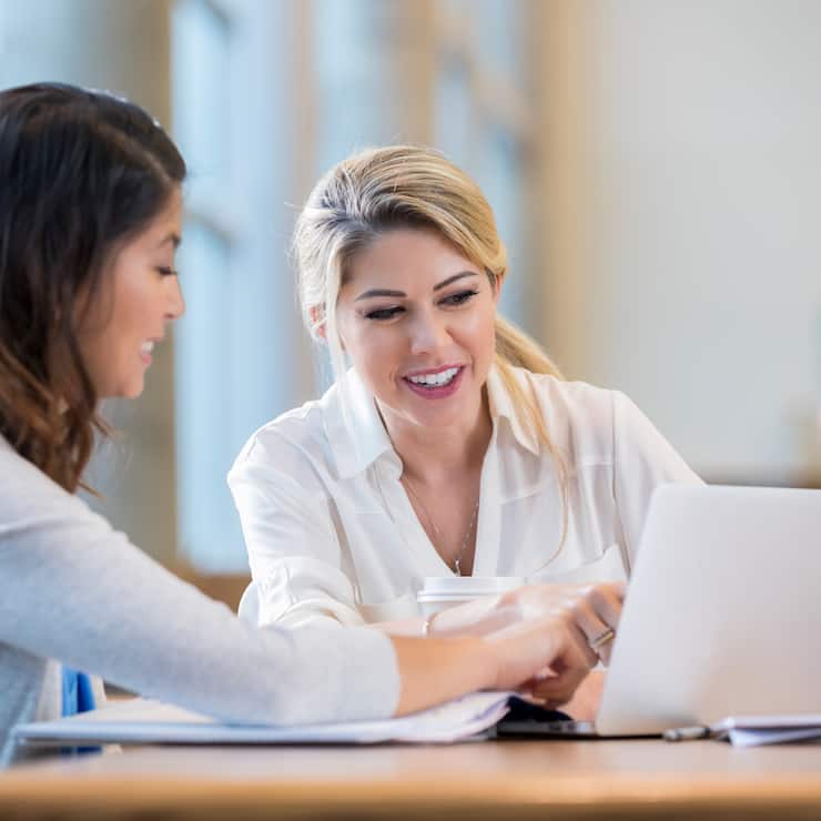 Diverse female college students review something on a laptop while studying for an exam.