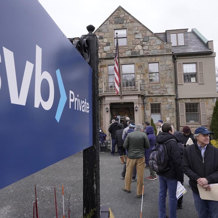 FILE - Customers and bystanders form a line outside a Silicon Valley Bank branch location, Monday, March 13, 2023, in Wellesley, Mass. The sudden crisis in the U.S. banking industry is sure to cause some tightening of lending and credit and a slowdown in the pace of borrowing and spending. If it does, the crisis could actually end up aiding the Federal Reserve in the elusive goal the Fed has been pursuing for a full year: A much lower inflation rate. (AP Photo/Steven Senne, File)