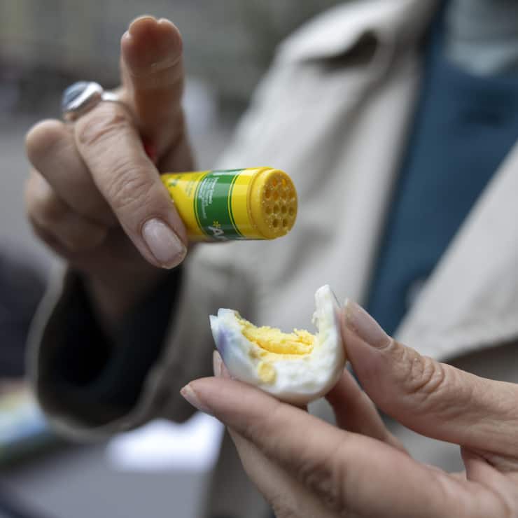 Eine Teilnehmerin streut Aromat ueber ihr Ei beim traditionellen Eiertuetschen am Ostersonntag, 31. Maerz 2024 in Bern. (KEYSTONE/Peter Klaunzer)