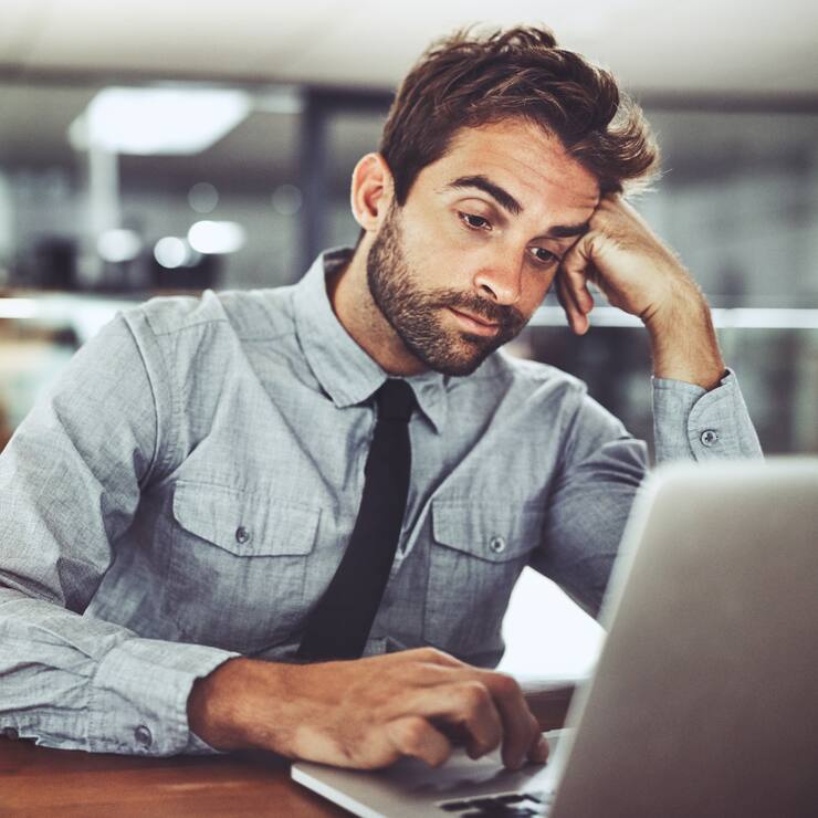 Shot of a handsome young businessman looking bored while working on a laptop in an office