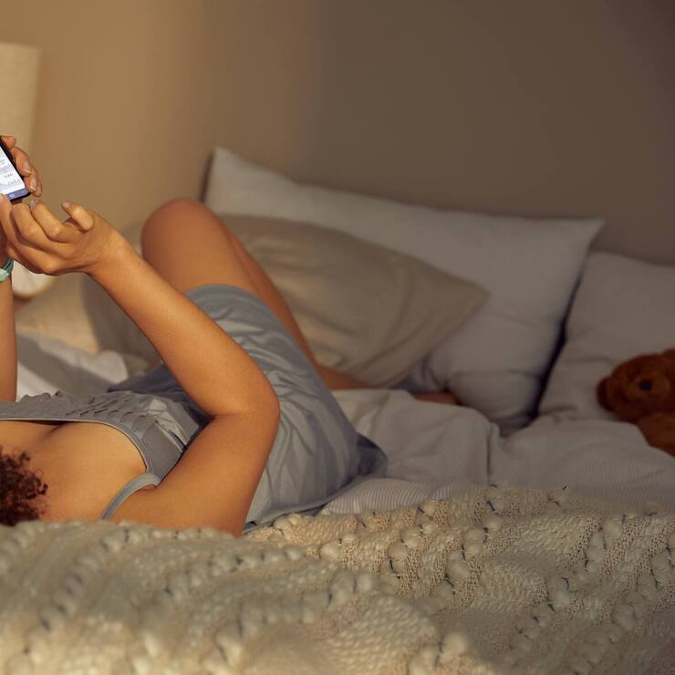 Frau liegt auf Bett mit Ava-Armbanduhr und schaut auf die Ava-App.