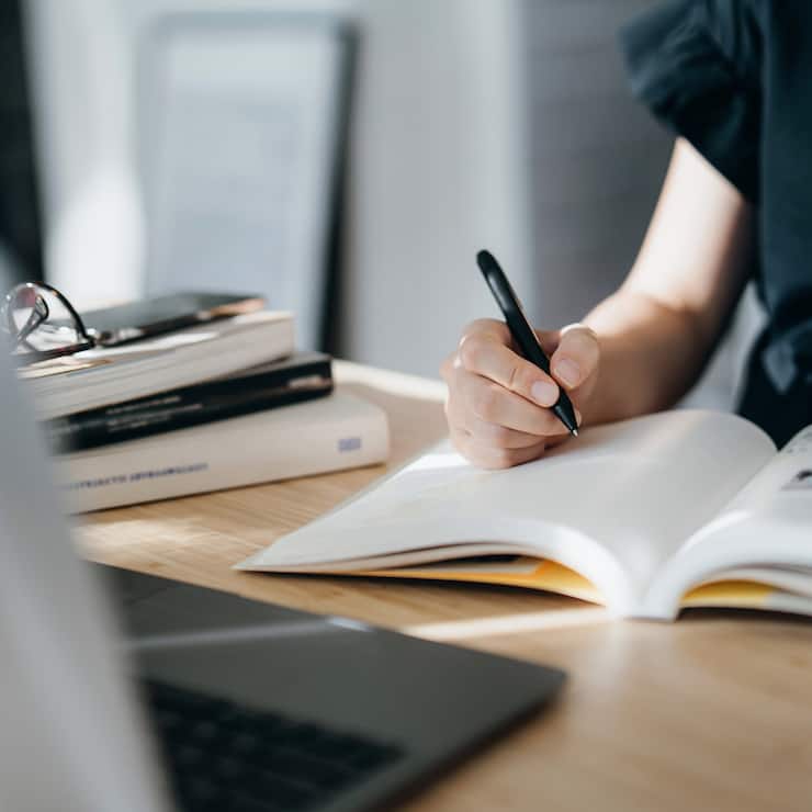 Cropped shot of focused young Asian woman reading book and making notes at home, concentrates on her studies. Further education, continuous learning concept