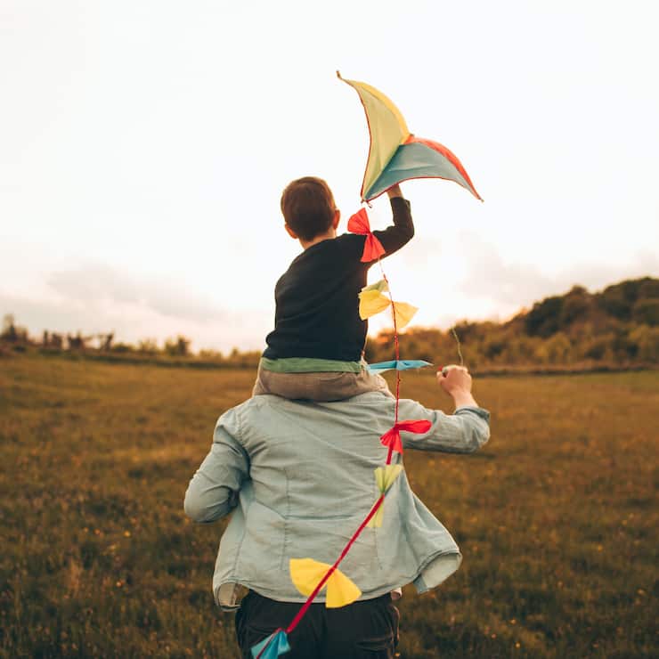 Little boy is running a kite with his father, on a beautiful day they are spending outdoors in nature
