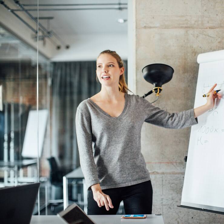 Confident businesswoman writing on flip chart in meeting at creative office