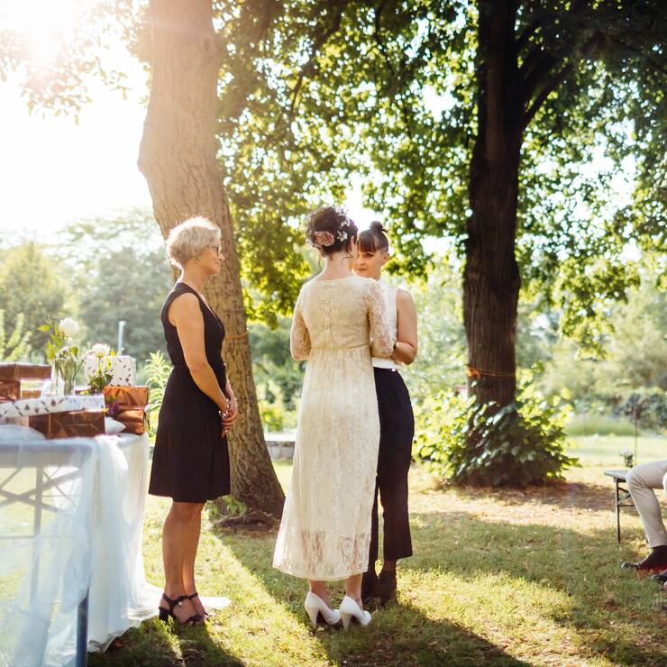 Lesbian couple holding hands in front of the altar. The wedding is outdoors and guest are seated in the foreground.