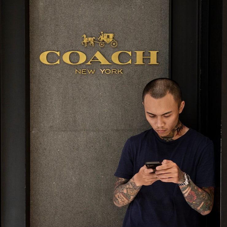 HONG KONG - 2019/04/08: A commuter seen using his smartphone outside of American multinational fashion and luxury accessories chain brand Coach store in Mong Kok shopping mall. (Photo by Budrul Chukrut/SOPA Images/LightRocket via Getty Images)