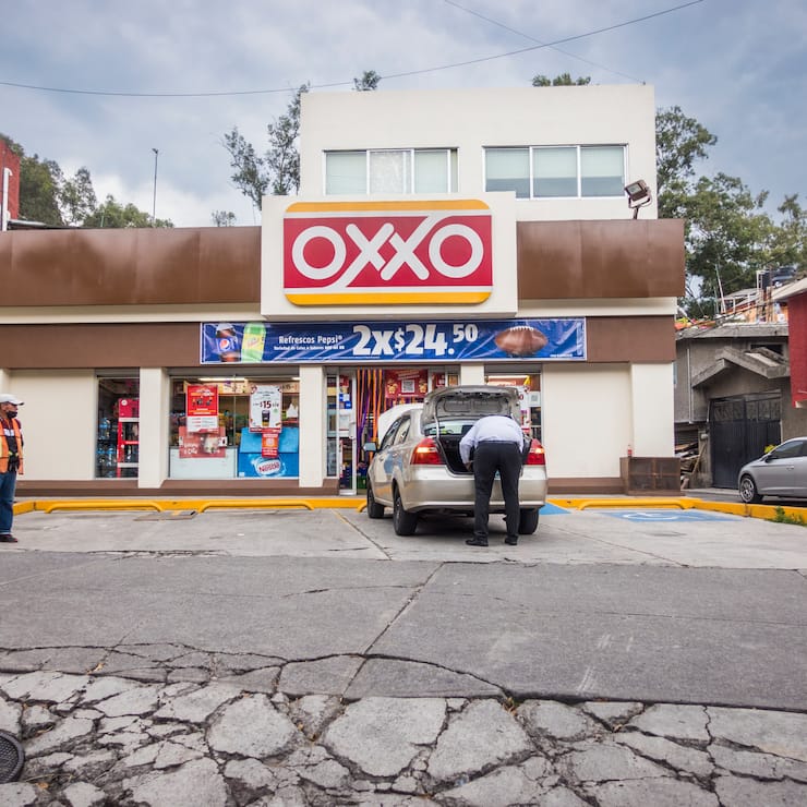 Mann packt Einkäufe ins Auto vor Oxxo-Laden
