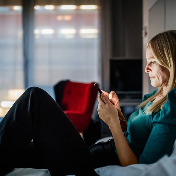 Businesswoman reclining on a hotel bed using her smartphone.