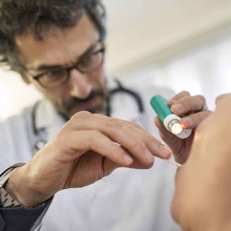 [EDITORS NOTE: POSED PICTURE] A doctor examinates throut and mouth of a patient, pictured on March 28, 2014. (KEYSTONE/Christian Beutler)