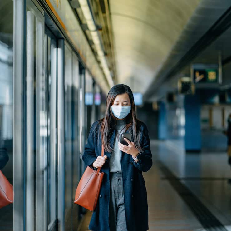 Asian woman with protective face mask using smartphone while walking on the subway platform