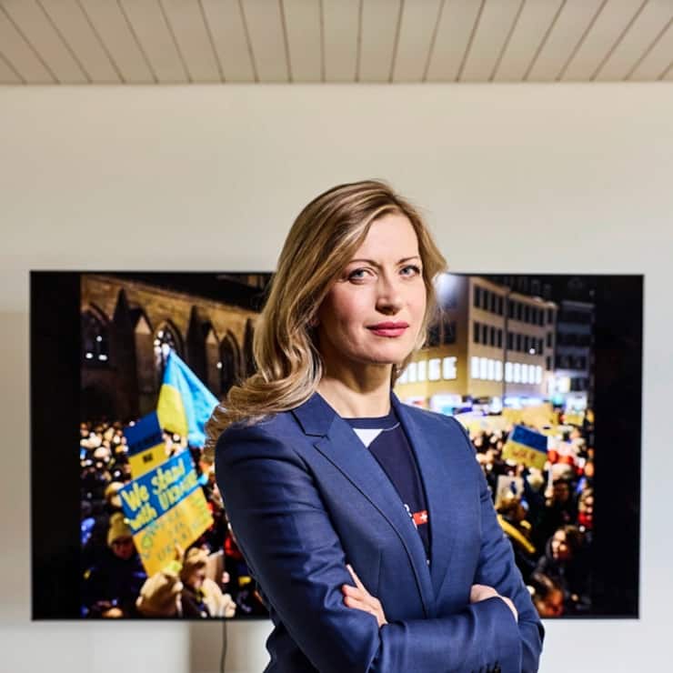 Die Ukrainerin Olga Feldmeier wurde von Forbes als "Krypto-Queen" gefeiert, nun bangt sie um ihre Familie und organisiert von ihrem Wohnort aus Hilfsaktionen. Im Hintergrund eine Aufnahme der Antikriegsdemo von ihrem Mann.