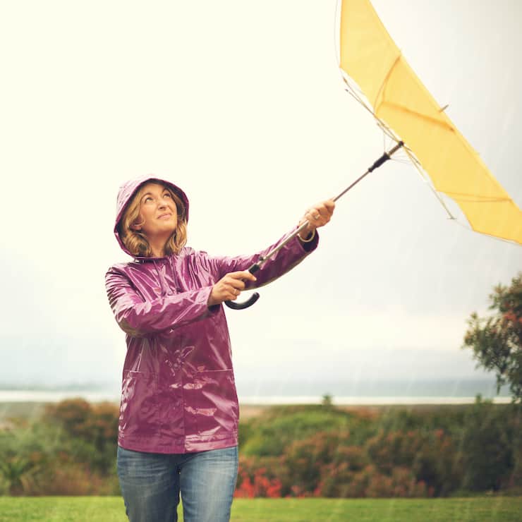 Shot of a woman standing outside in the rain holding an umbrella looking up in the sky